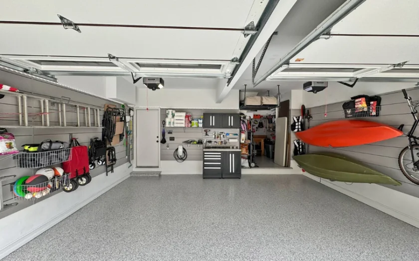 Finished two-car garage with a gray flake floor, slatwall storage, cabinets and kayaks hung on the wall